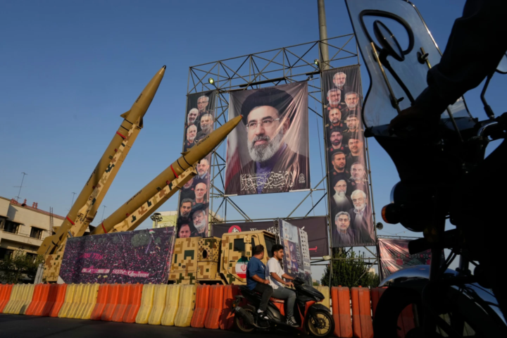 Motorbikes drive past Iranian missiles and banners showing portraits of the Iranian Supreme Leader Ayatollah Mojtaba Khamenei, center, and the late armed forces commanders and nuclear scientists, who were killed in Israeli and U.S. strikes, displayed in a military exhibition commemorating the anniversary of the start of the 1980-88 Iraq-Iran war at Baharestan Square, in Tehran, Monday, Sept. 28, 2026. (AP Photo/Vahid Salemi)